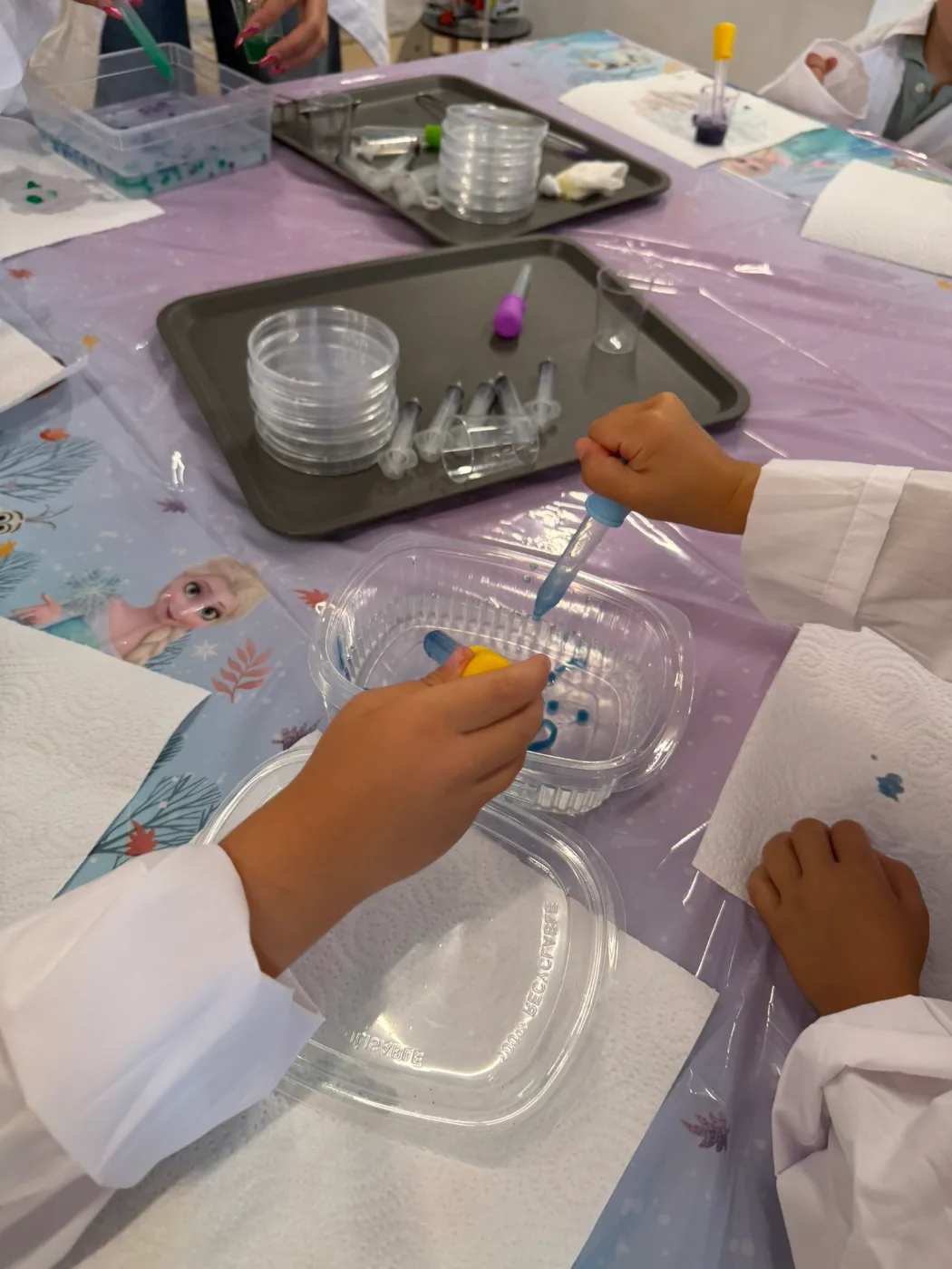 Manos de niños con pipetas echando gotas azules en un recipiente